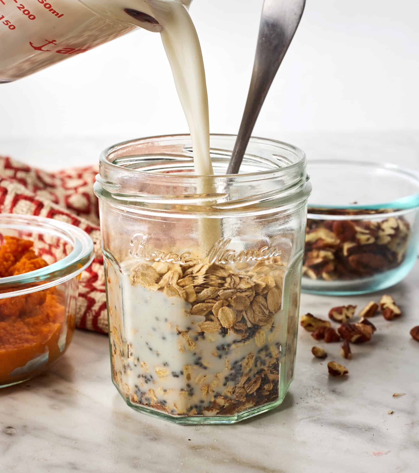 Pouring almond milk into jar with oats, chia seeds, and spices