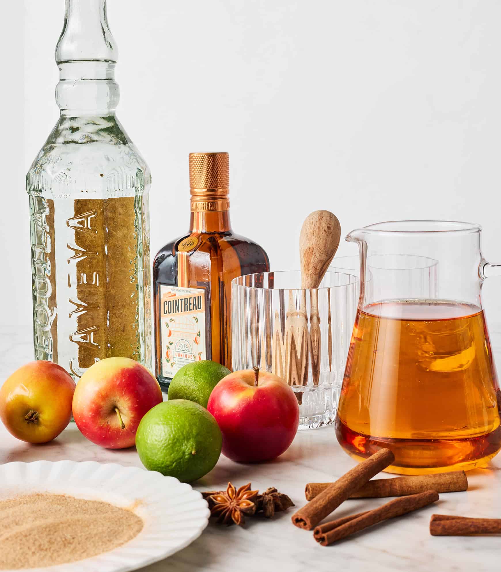 Apple cider, tequila, Cointreau, fresh apples, limes, and spices on countertop