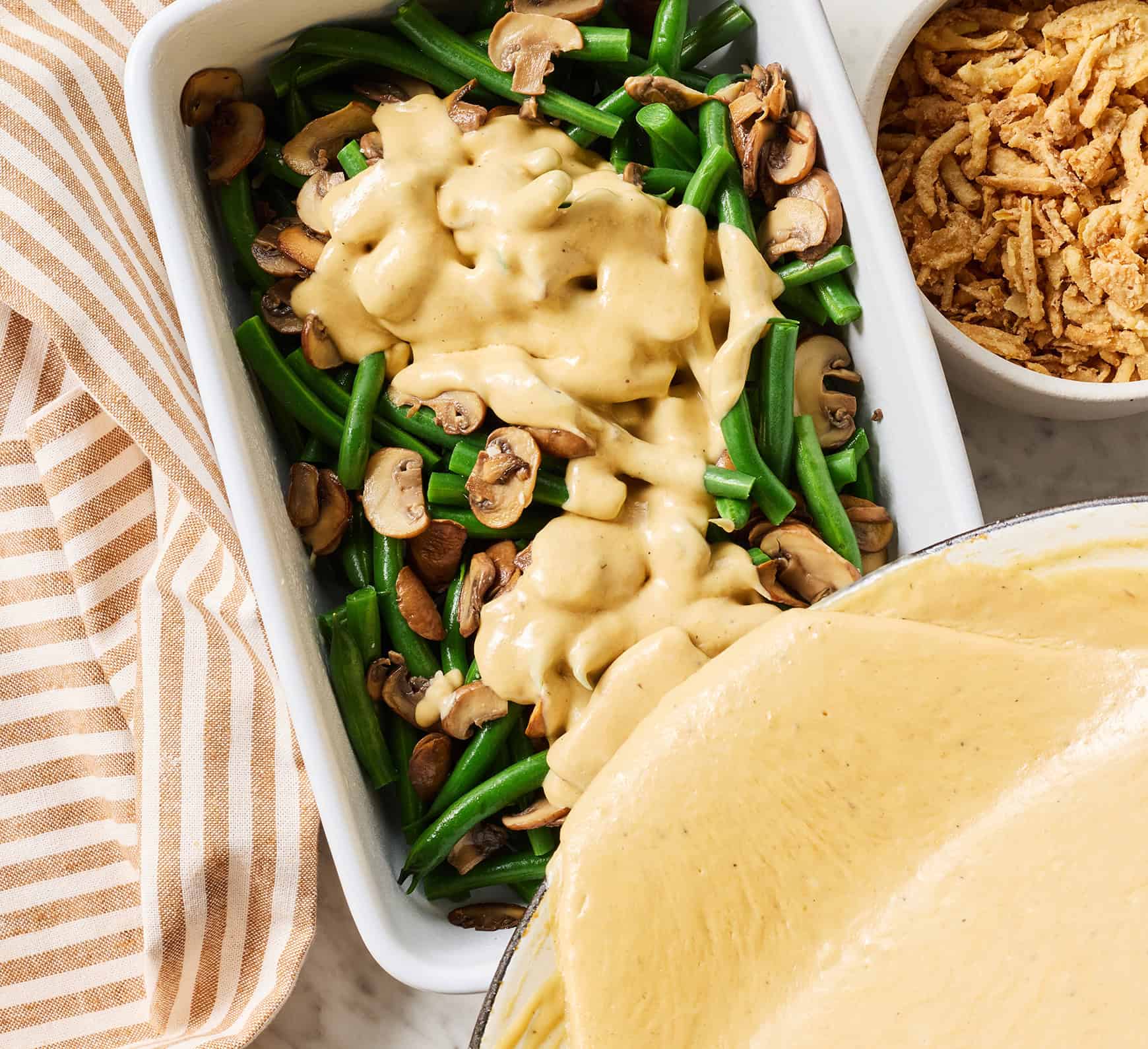 Pouring sauce over green beans and mushrooms in casserole dish