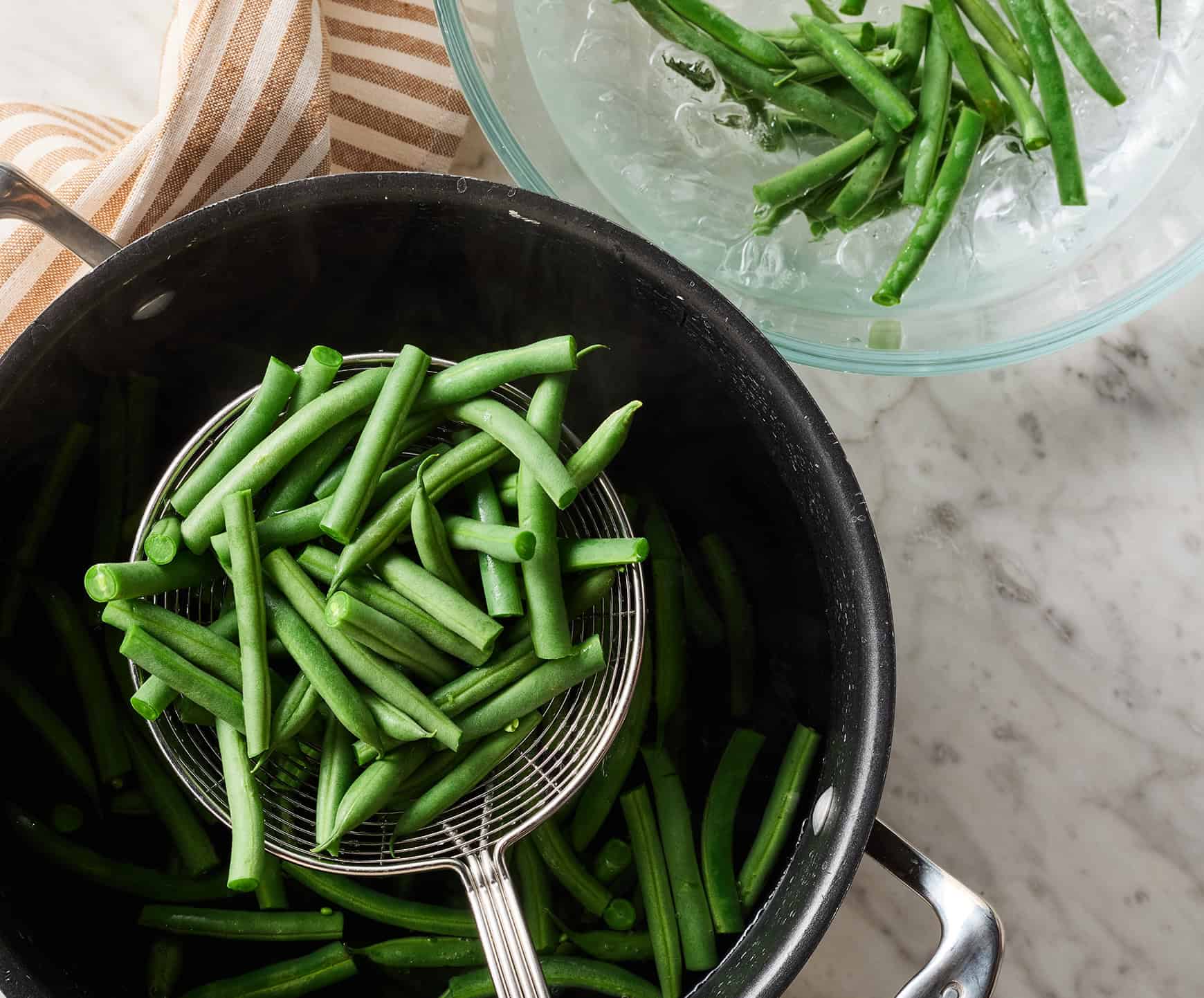 Scooping blanched green beans out of boiling water and into ice water